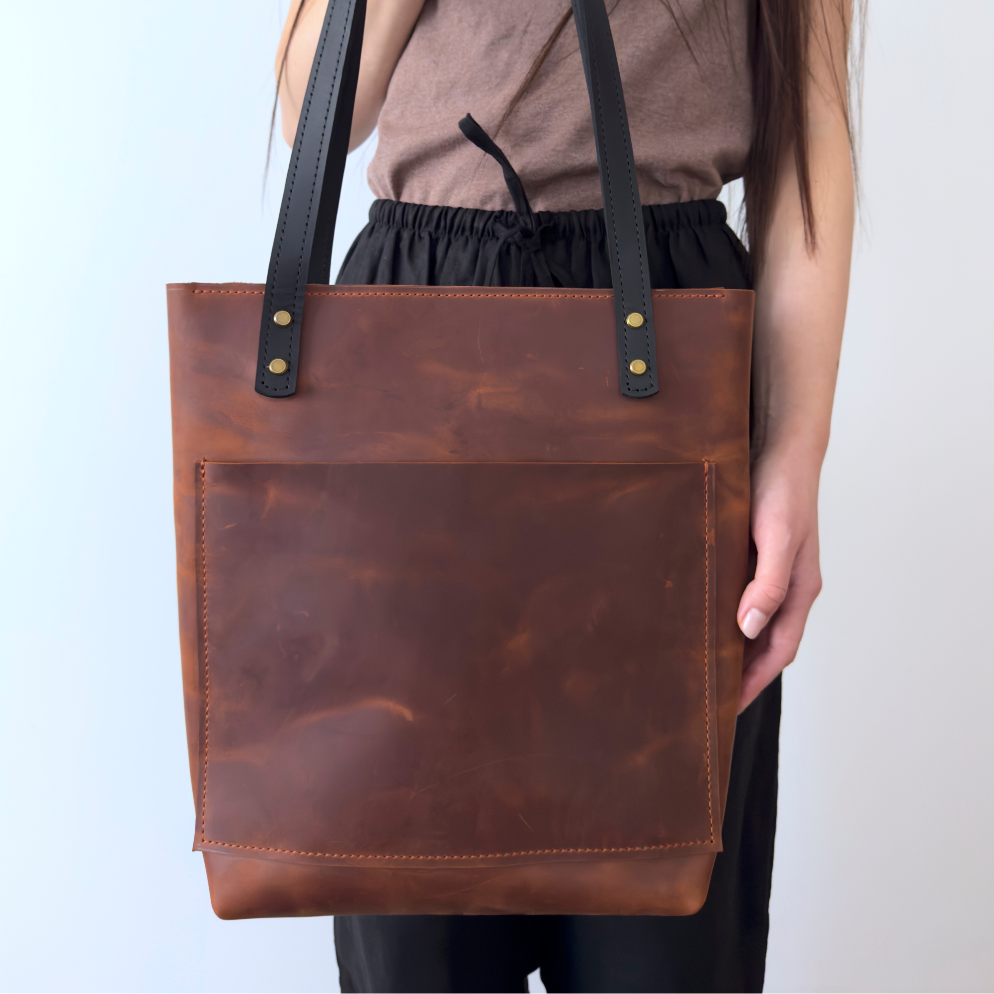 Brown leather tote bag held by a person against a light background